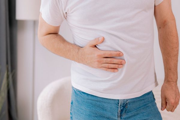 Hombre con la mano en la parte superior derecha del abdomen. Sufre dolor compatible con hígado graso.