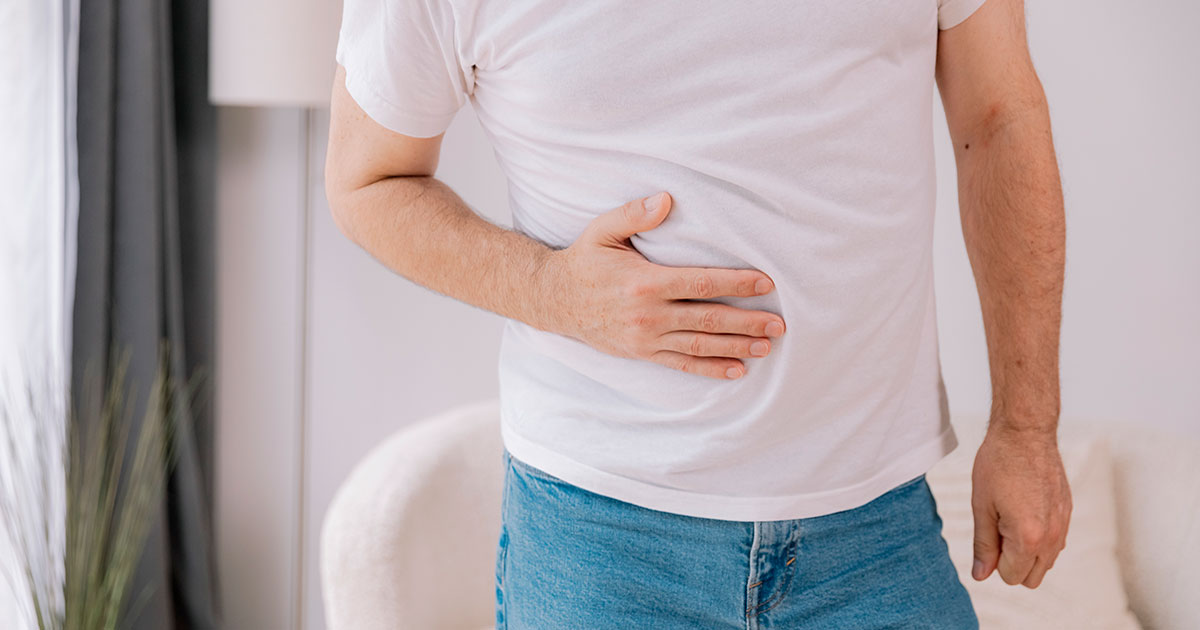 Hombre con la mano en la parte superior derecha del abdomen. Sufre dolor compatible con hígado graso.